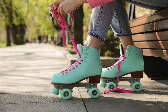 Woman lacing roller skates while sitting on bench outdoors, closeup