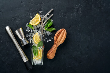 Mojito or Lemonade cocktail in highball glass with ice cubes, mint and lime on black stone...