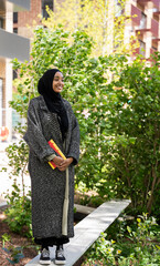 Black Muslim woman standing in park with a book in hand