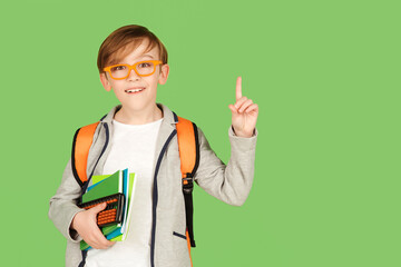 Cute student boy with school bag over green background. Happy kid in glasses pointing up on empty copy space. - Powered by Adobe