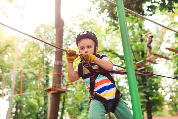 Cute boy climbing the high rope course in adventure park. Kid in safety helmet, extreme sport.