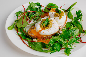 Avocado egg benedict with cream cheese Philadelphia. Poached eggs on healthy bread toast with hollandaise sauce. Cut egg. The yolk flows out. Green salad arugula leaves.