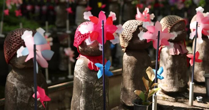 A slow motion of moving colorful windmills with Jizo statue daytime closeup