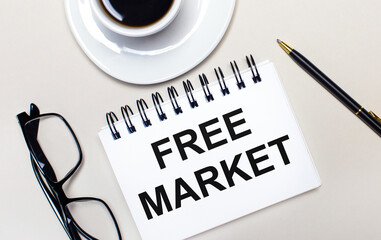 Glasses, a white cup of coffee, a white notebook with the words FREE MARKET and a ballpoint pen lie on a light background. Flat lay. View from above.
