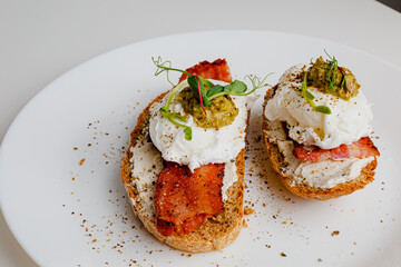 Avocado eggs benedict with pesto sauce, grilled bacon, pepper, cream cheese Philadelphia. Poached eggs on healthy bread toast with hollandaise sauce. Cut egg. The yolk flows out. Micro greens. 