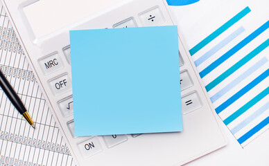 On the desktop is a white calculator with a blue blank sticker with a place to insert text, a pen and blue reports. Business concept