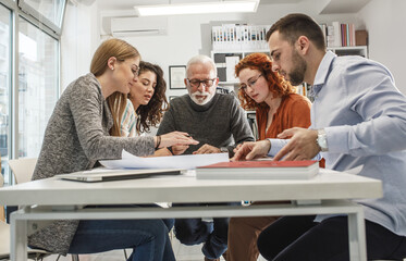 Working day in a design studio.Group of designers and architects discuss about new project.They sitting at the desk and looking at the blueprint.	
