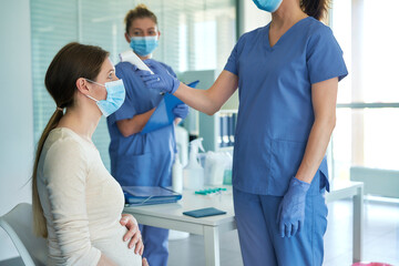 Female doctor measuring fever to a pregnant woman