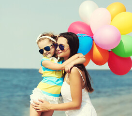 Happy mother and little girl child with colorful balloons on a beach over a sea background