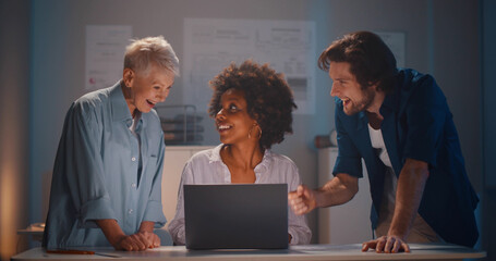 Group of happy diverse business people team working on project using laptop in office at night