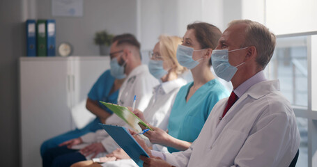 Doctors and interns in protective mask listening to professor in conference room - Powered by Adobe