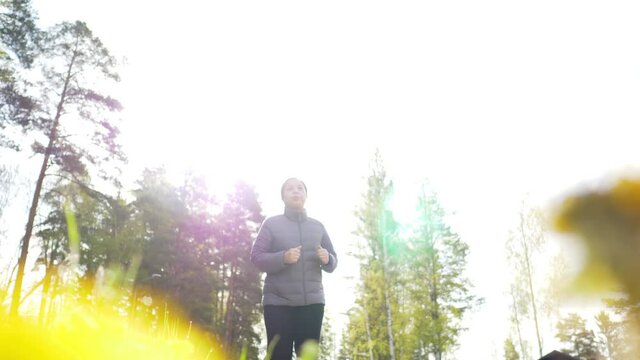 Low angle shot of Asian woman wearing coat and going jogging in the forest to see a beautiful nature in the morning, morning walk with sunlight, stuning view outdoor on the weekend, running exercise