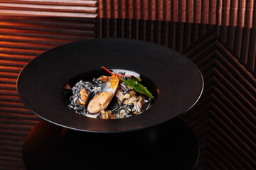 black spaghetti pasta with cuttlefish ink, mussels and red caviar in a beautiful black plate on a dark texture background. close-up. space
