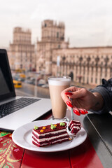 Girl eating piece of cake and cup of latte coffee in a cafe on the blur background of city