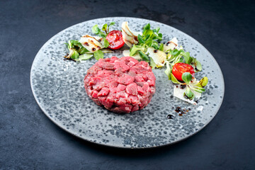 Modern style gourmet tartar raw from beef filet with lettuce, tomatoes and parmesan as close-up on a Nordic design plate with copy space