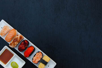The sushi set is a famous Japanese dish, put on a ceramic plate, beautifully arranged on a black background.