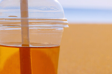 Cold drink in plastic glass with paper cocktail straw on blurred sea and sand background 