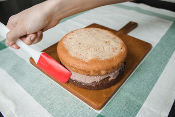 Young woman is preparing small cake at home. It consists of two sponge cakes and a cream layer in between, chocolate ganache with grated bitter chocolate. Series of photos with a step-by-step recipe