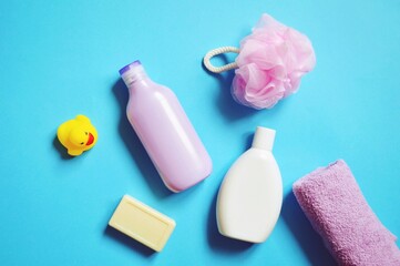 Moisturizing body lotion for sensitive skin and natural organic shampoo, soap, sponge, rubber duck on a blue background. Flat lay toiletries essentials