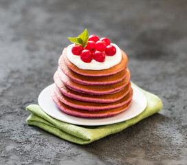 Berry pancakes with cream on a plate on a linen napkin on a dark gray background