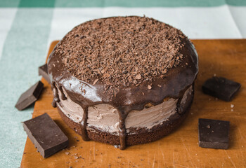A fresh homemade cake is on a wooden board. Two sponge cakes and a cream layer in between covered with chocolate ganache and grated bitter chocolate. The process of making a cake at home