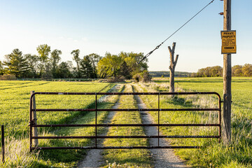 An iron gate on a farm lane in the spring with a no trespassing sign. - obrazy, fototapety, plakaty