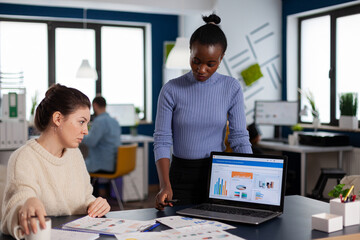 Diverse businesswomen discussing new project for company evolution, black woman checking tasks on new contract. Multiethnic employees gathered in co-working space.