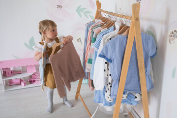A little girl chooses clothes and puts things in order in the room, a child tries on dresses in a bright children's room