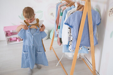 A little girl chooses clothes and puts things in order in the room, a child tries on dresses in a bright children's room