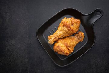 crispy fried chicken drumstick with black pan on the dark tone texture background with copy space for text