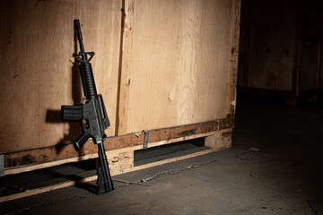 M4 carbine machine gun leant up against a wooden crate with dramatic lighting and shallow depth of...