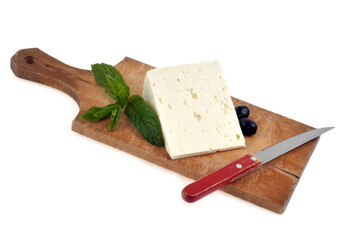 Morceau de feta sur une planche à découper avec un couteau, des olives noires et des feuilles de menthe en gros plan sur fond blanc