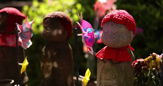 A slow motion of moving colorful windmills with Jizo statue daytime closeup