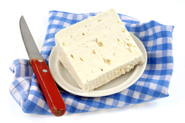 Morceau de feta dans une soucoupe posée sur une serviette à carreaux à côté d'un couteau en gros plan sur fond blanc