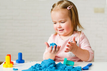 Little girl playing with blue kinetic sand. Educational games with children for fine motor skills....