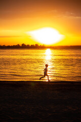 Child running at orange sunset near the water, silhouette of a man 