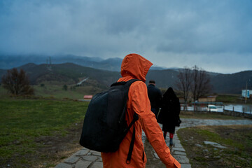 A person in an orange raincoat with a backpack walks in the rain in the mountains