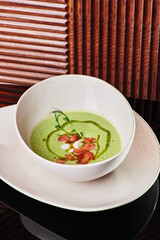 Green cream spinach soup decorated with tomatoes and mushrooms in a beautiful white plate. Dark textured background. Close-up. Space