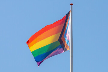 Worldwide LGBTQ community concept with progress pride flag (new design of rainbow flag) waving in the air with blue sky, Celebration of gay pride, The symbol of lesbian, gay, bisexual and transgender.