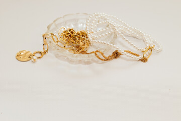 Gold jewelry, blastets and a chain with beads and pearls in a crystal stand on a gray background. Business content.