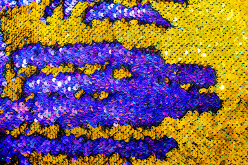 The shiny bright texture of the sequins changes color. Purple and yellow. Fabric for fancy dresses.