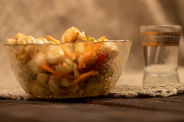 Pickled mushrooms in a glass dish and a mug of beer on a table covered with a homespun cloth with a...