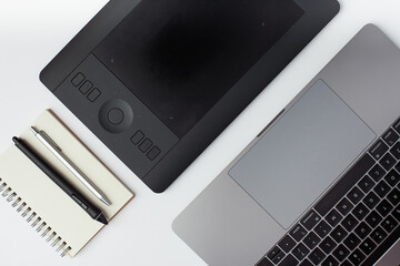Top view photo of a, notepad, pen, graphic design tablet, stylus and a laptop on a white background.