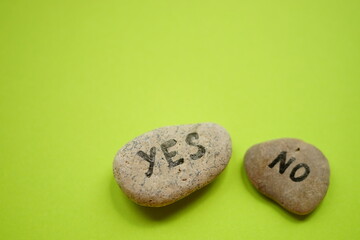 Obraz na płótnie Canvas Two pebbles with yes and no text on them. Green table