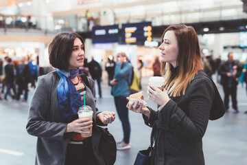 Two young women having coffee to go indoors having fun together