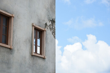part of the wall of a house with a window through which the sky is visible in the left half of the photo the sky in the right half of the photo.