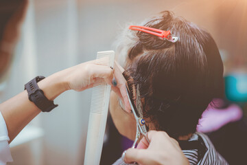 Fototapeta premium Asian woman barber wears green mask cut black, white hair old customer. beautiful hairstylist trimming with scissors in haircut. female Hairdresser working in Thai stylist beauty salon