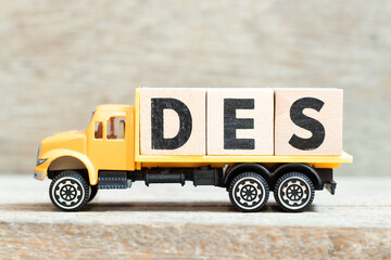 Toy truck hold alphabet letter block in word DES (Abbreviation of Delivered Ex Ship) on wood...