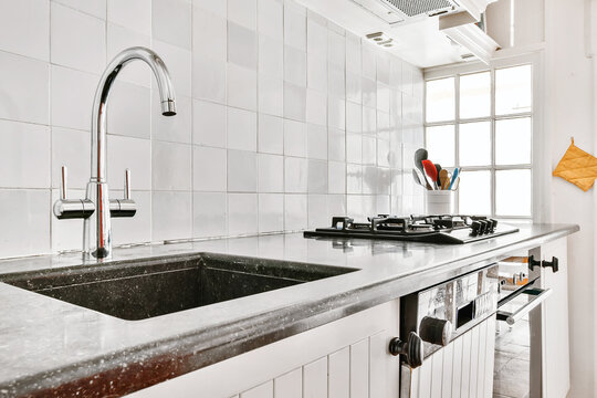 Sink with shiny tap installed under modern counter near jar with spices and gas stove in kitchen at home