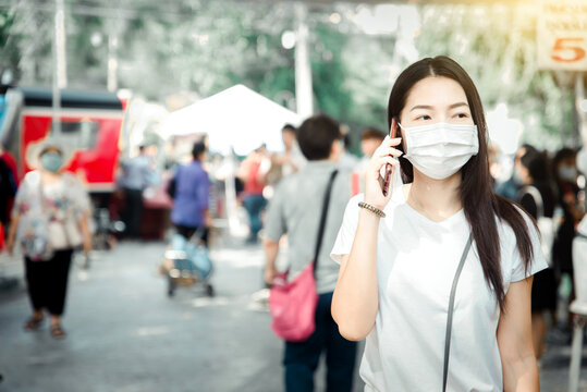 beautiful asian woman wear white mask to protect against dust PM 2.5 and viruses when going out for shopping in Thailand. pretty girl use mobile phone in outdoor.soft focus and blurry background
